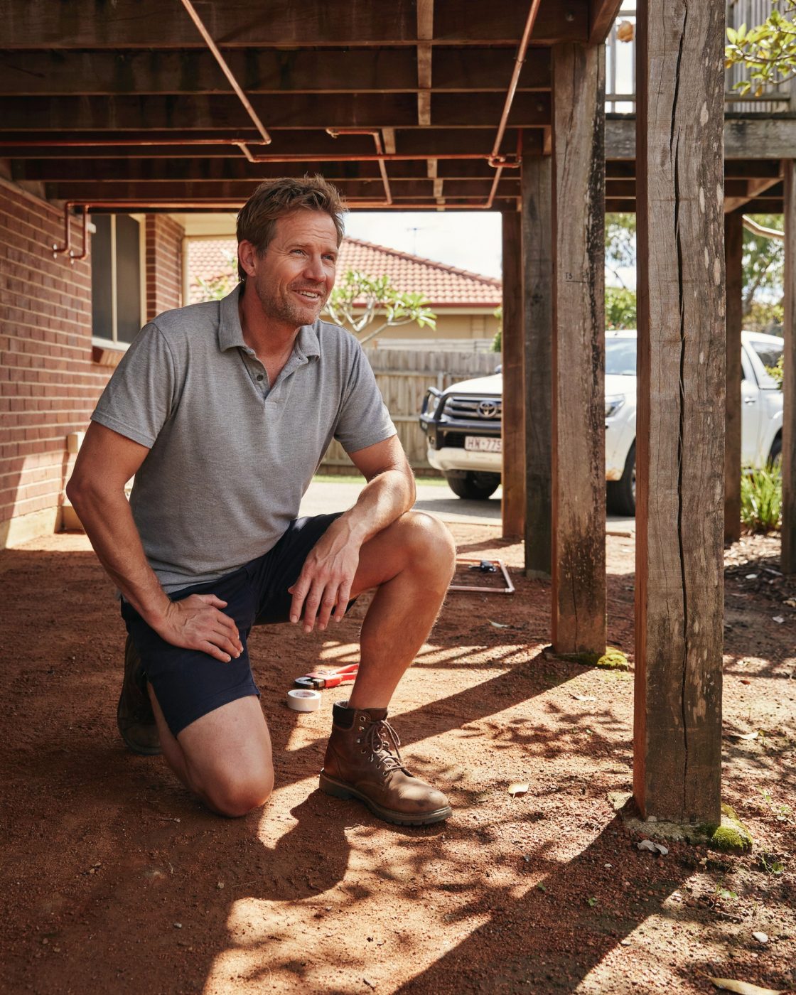 Harbour Plumbing tradesperson crouching beside copper pipework under a Brisbane home