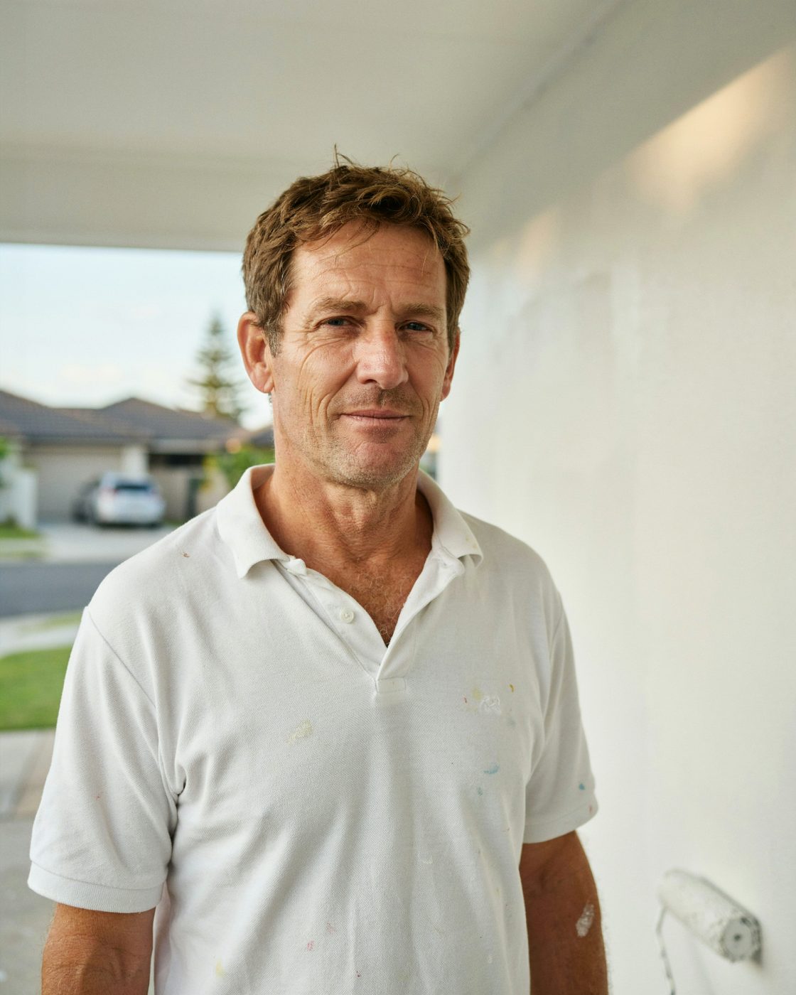 Painter standing beside a freshly painted rendered home exterior